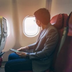 Man holding a magazine looks out airplane window.