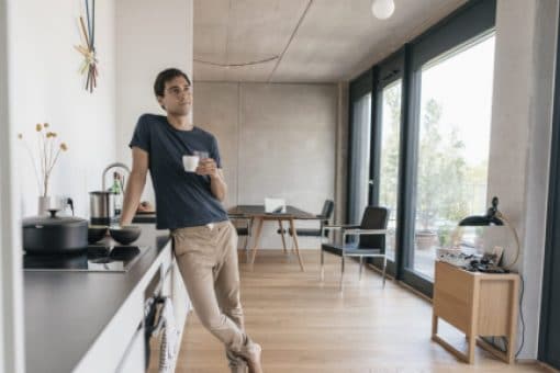 Man drinks coffee leaning against his kitchen counter.