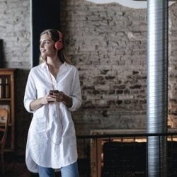 A woman with headphones holds her phone while standing in a rustic building.