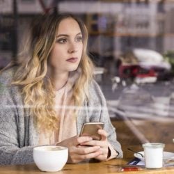 Woman sits in restaurant looking out window and holding mobile phone.