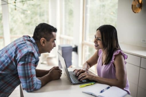 Couple speaks to one another as wife types on laptop