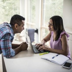 Couple speaks to one another as the woman types on a laptop