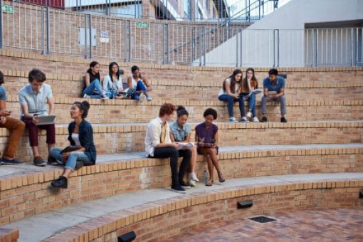 Groups of young adults sit on steps in an outdoor brick amphitheater.