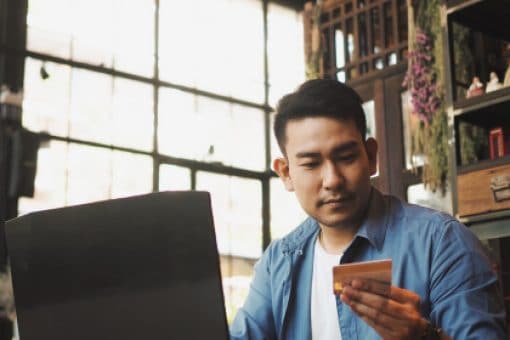 Man using laptop looks at credit card in his hand