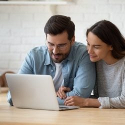 Happy couple sits together as they look at the screen of their laptop