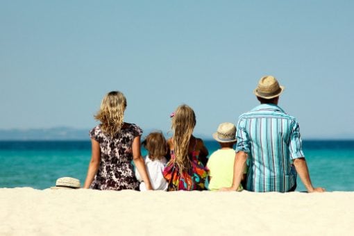 A couple and their 3 kids sit on the sand at a beach looking at the ocean