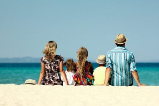Having used their new credit card, a couple and their three kids sit on the sand at a beach looking at the ocean.