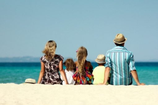 A couple and their 3 kids sit on the sand at a beach looking at the ocean