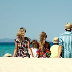 A couple and their three kids sit on the sand at a beach looking at the ocean.