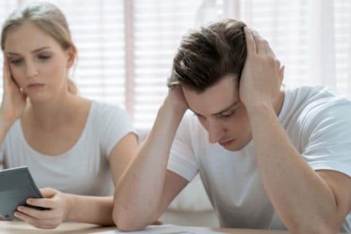 A young couple is distressed looking at a calculator.