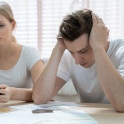 A young couple is distressed looking at a calculator.