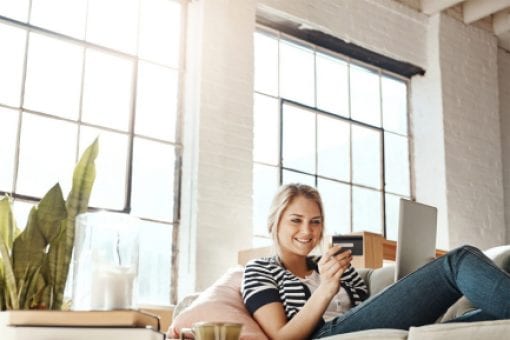 Young woman reclines on couch holding a credit card and digital tablet.