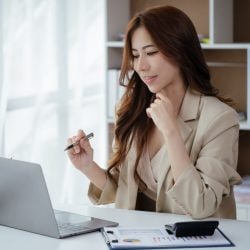 Professional woman holds a pen as she works on laptop
