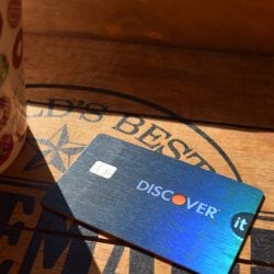 A shiny blue Discover it® Credit Card lays on a wooden restaurant table in the sun.