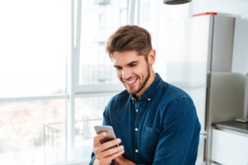 A man looks down at the cell phone he’s holding.