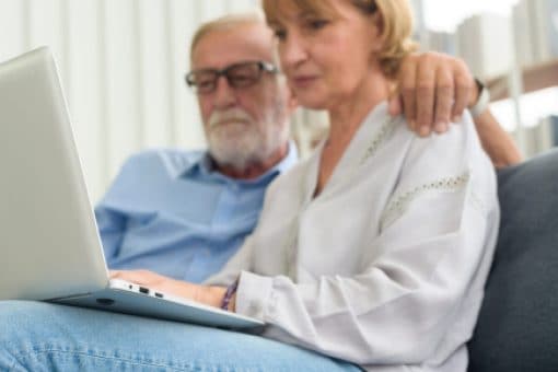 Senior couple using laptop sitting on a couch