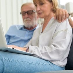Senior couple using laptop sitting on a couch.