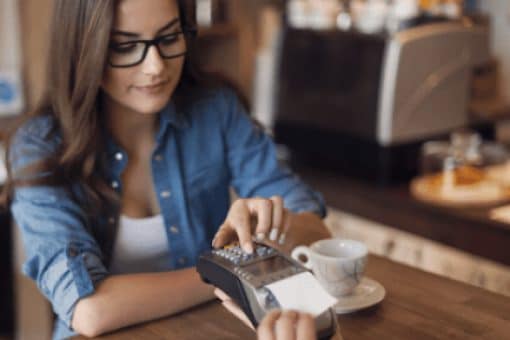 Young woman paying in cafe by credit card reader