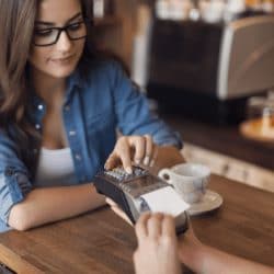 Young woman paying in cafe by credit card reader.