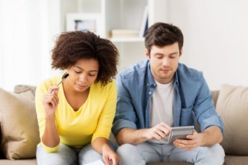 Couple Sitting on Couch Reviewing Papers, Money And A Calculator