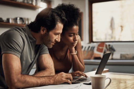 A couple sharing a laptop that sits on a table next to paperwork