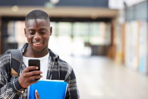 A young, Black, male college student reads messages on mobile phone.