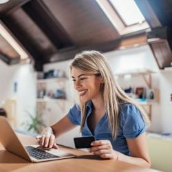 Young woman smiling at laptop with credit card in hand