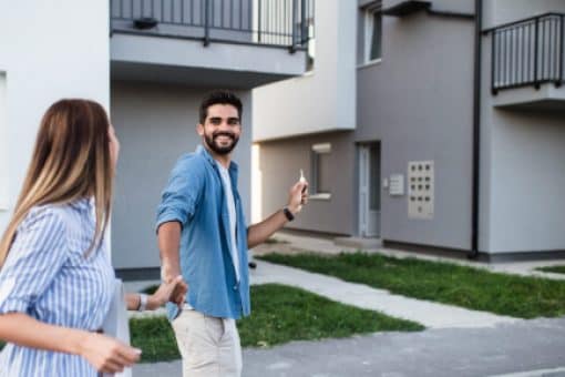 Young couple in front of an apartment building holding keys.