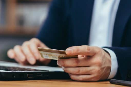 Man in suit holds credit card and types on laptop