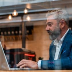 A man works on laptop near a cafe window.