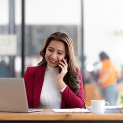 A woman talks on her cell phone while browsing on her laptop.