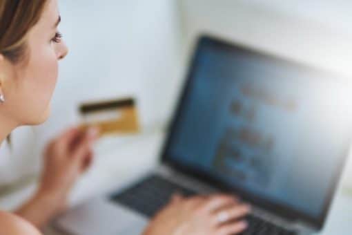 Image of a young woman holding a credit card and using a laptop.