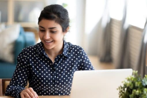 Young woman sits in front of her laptop while excitedly typing on a calculator.