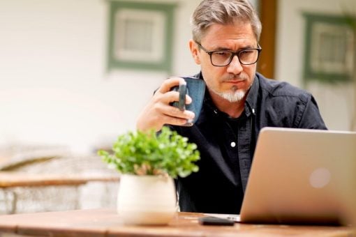 Middle-aged man works on laptop and holds coffee cup