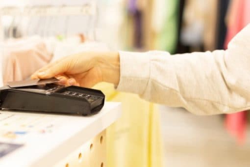Hand taps credit card against pay terminal in clothing store