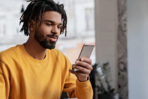 A young man, holding a credit card in one hand, looks contentedly at the phone in his other hand.