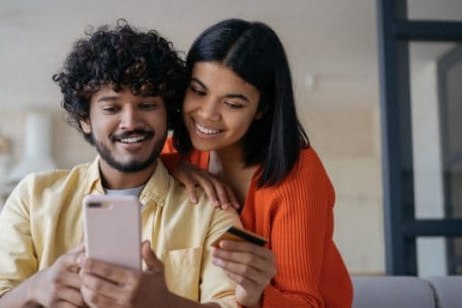 Smiling couple stares at the phone in the man’s hand while the woman holds a credit card.