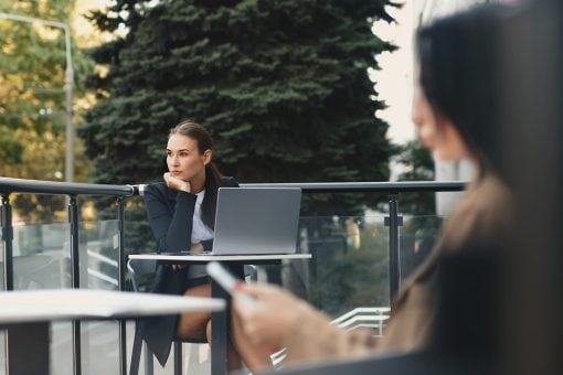 Woman sits outside at a table looking away from her laptop