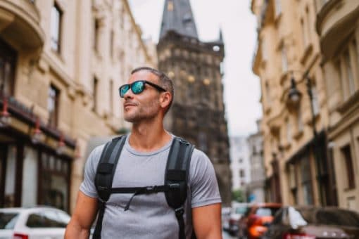 Man in sunglasses wearing backpack walks down European street