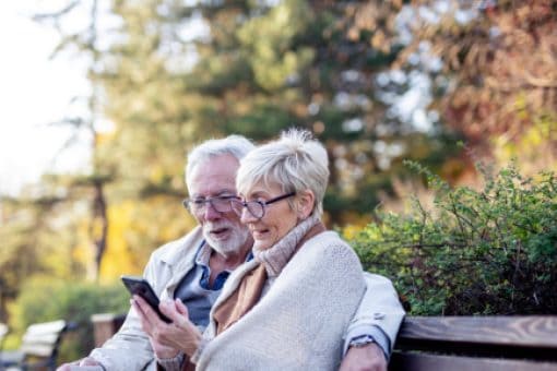 Senior couple sits on a park bench holding a credit card and staring at a cell phone.