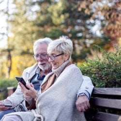 Couple sits on a park bench holding a credit card and staring at a cell phone.