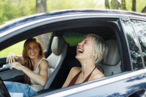 Two women sit in a car talking and laughing