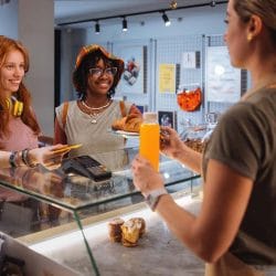 Two women standing in a bakery hand payment to the cashier.