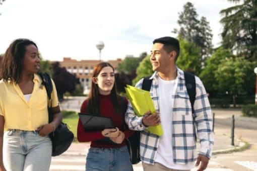 A group of three students with backpacks walks through a college campus.