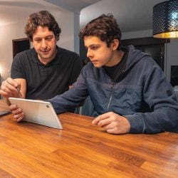 A father and teenage son look at a tablet screen together to compare credit cards.