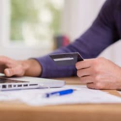 Man uses laptop and holds a credit card.