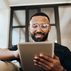 Man wearing glasses uses a tablet device in a well-lit room.