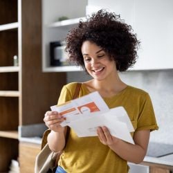 Happy woman smiling while looking at mail upon arriving home.