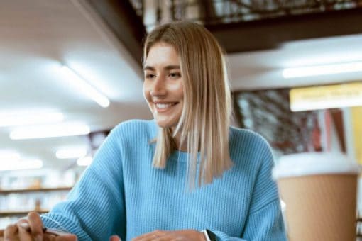 A woman in a library smiles as she types on a laptop.