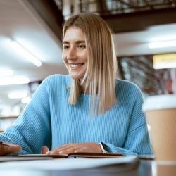 A woman in a library smiles as she types on a laptop.
